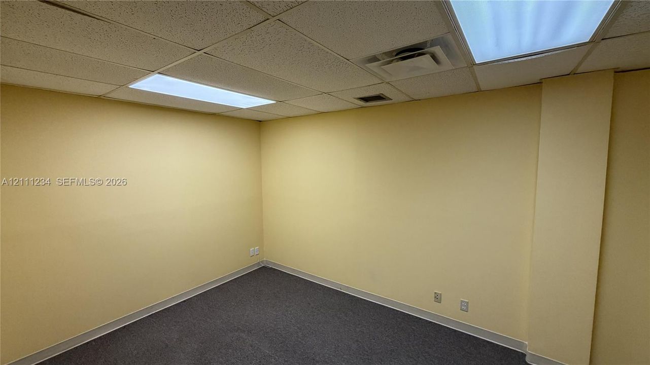 Interior room featuring neutral wall finishes, dark carpeting, and a drop ceiling with recessed rectangular lighting