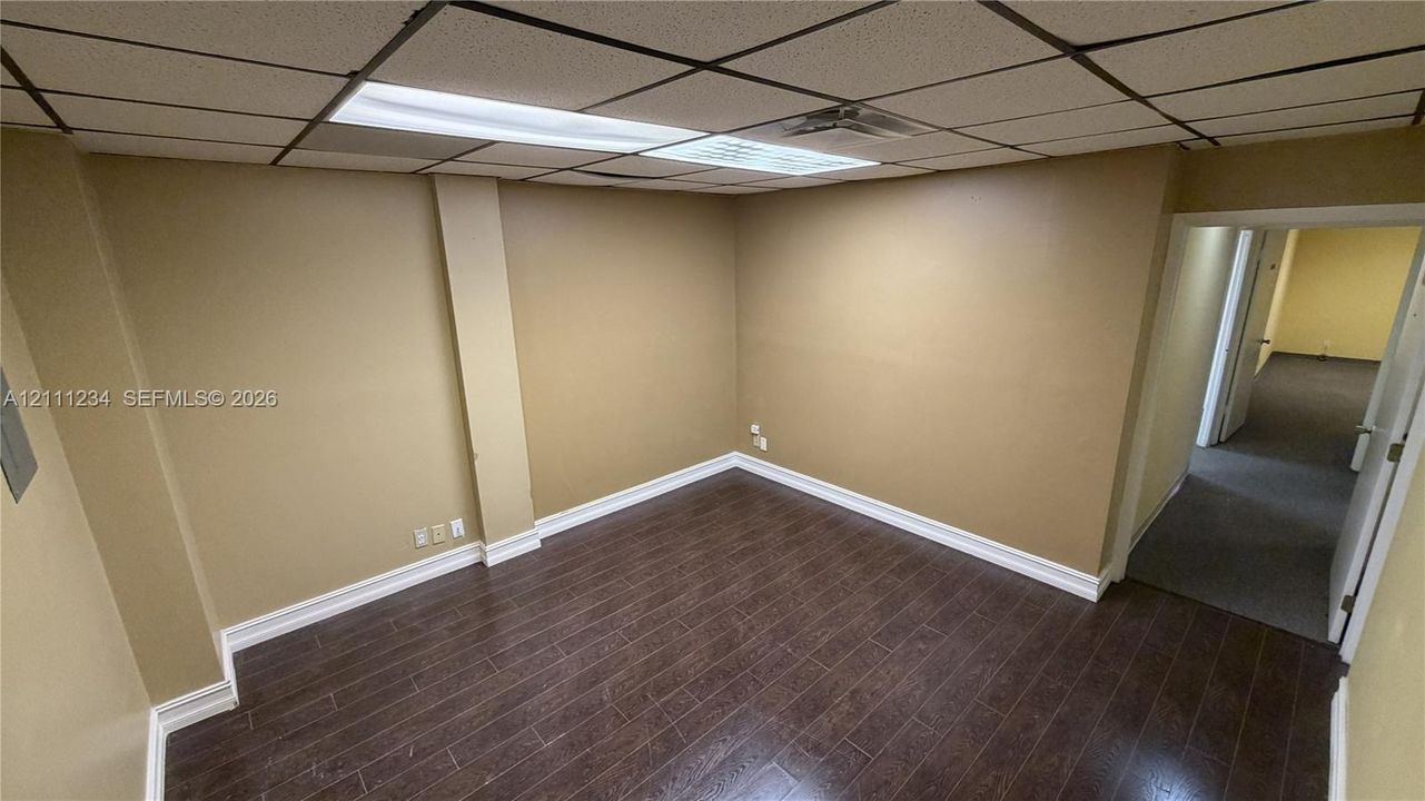Interior room featuring dark wood-finish flooring, neutral wall paint, and a dropped grid ceiling with integrated rectangular lighting