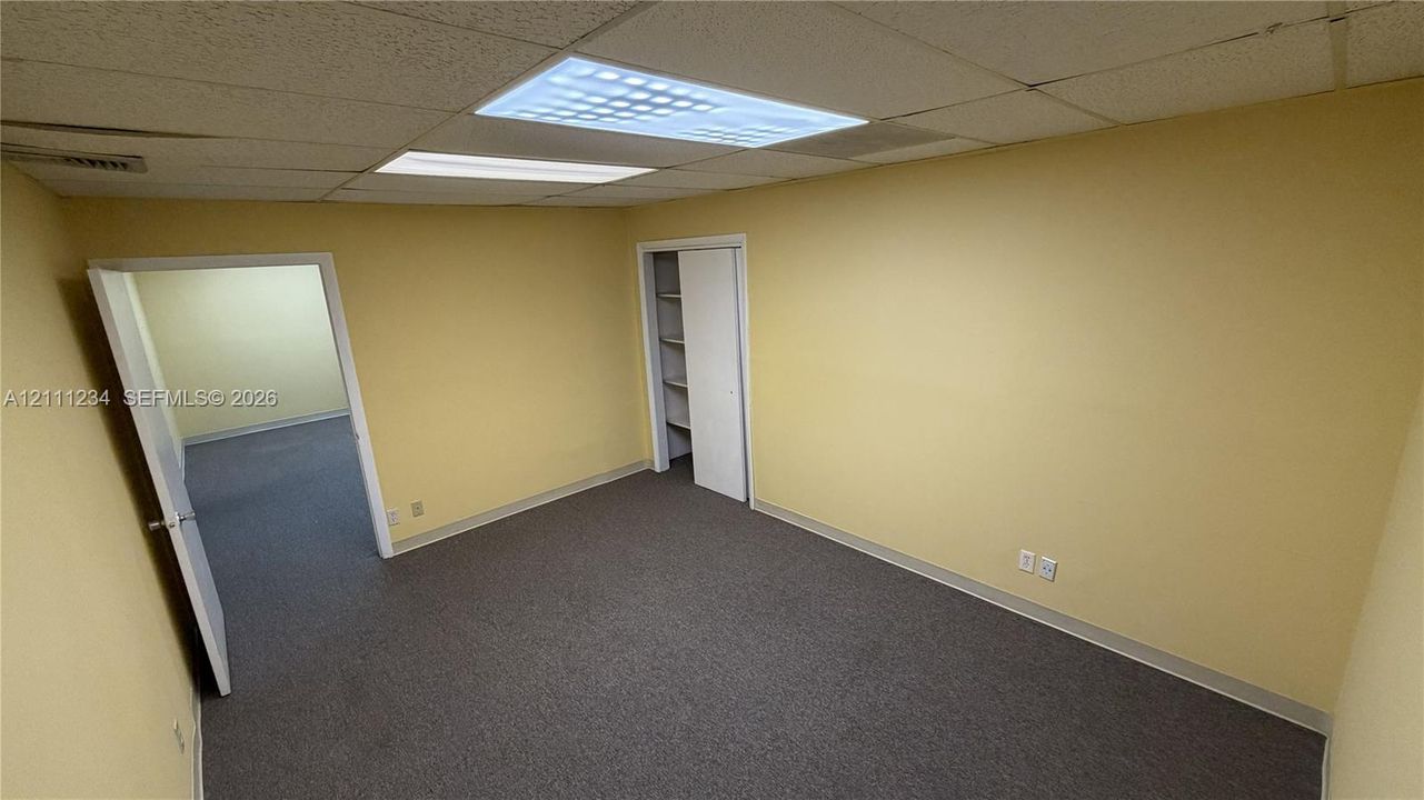 Interior room featuring gray carpeting, drop ceiling with recessed lighting, and a closet with built-in shelving