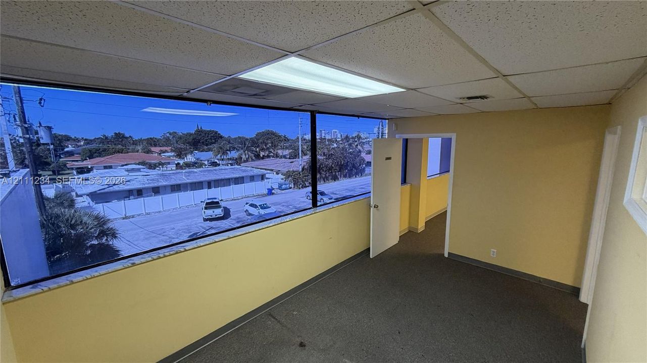 Expansive wall-to-wall windows, dropped acoustic tile ceiling, recessed fluorescent lighting, and commercial-grade carpeting