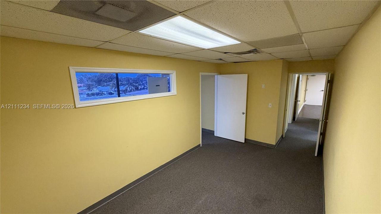 Interior room featuring carpeting, a horizontal rectangular window, a drop ceiling with recessed lighting, and multiple interior doors