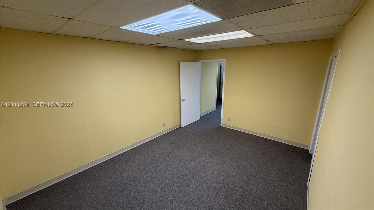 Interior room featuring gray carpeting, a suspended ceiling with recessed rectangular lighting, and two interior doors