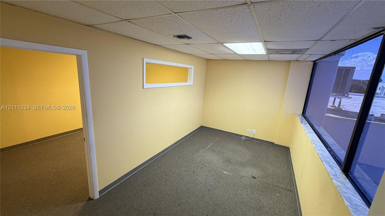 Interior space featuring a large floor-to-ceiling window, drop ceiling with integrated lighting, wall-to-wall carpeting, and a horizontal accent window