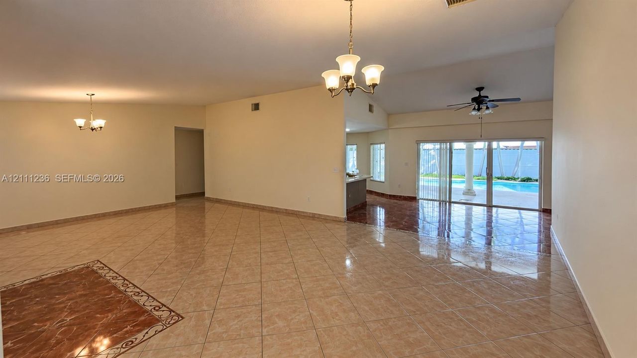 Open interior featuring high vaulted ceilings, tiled flooring with decorative inlays, multi-arm chandeliers, and sliding glass doors with access to an exterior pool area