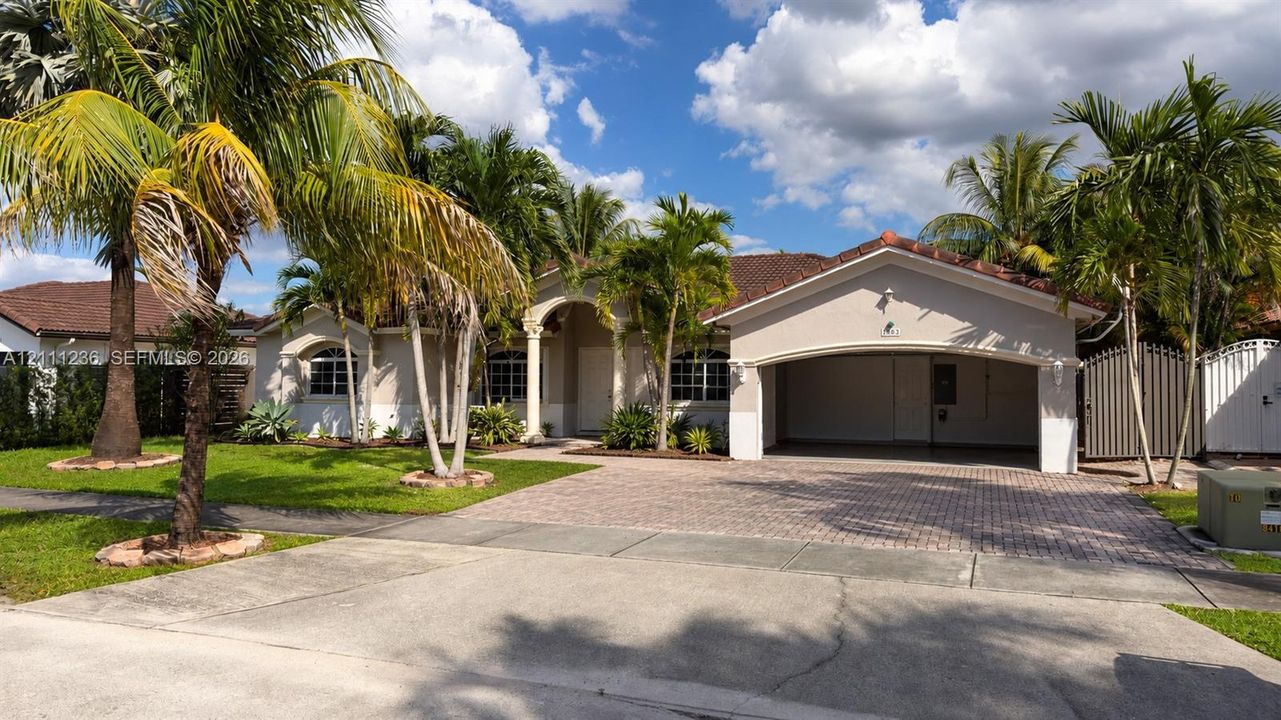Single-story exterior featuring a recessed entryway with arched architectural detail, multi-car paver driveway, integrated carport, and mature landscaping