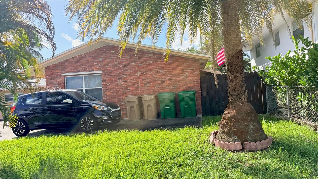 Exterior featuring a brick facade, concrete driveway, and mature palm tree with stone-style landscape edging