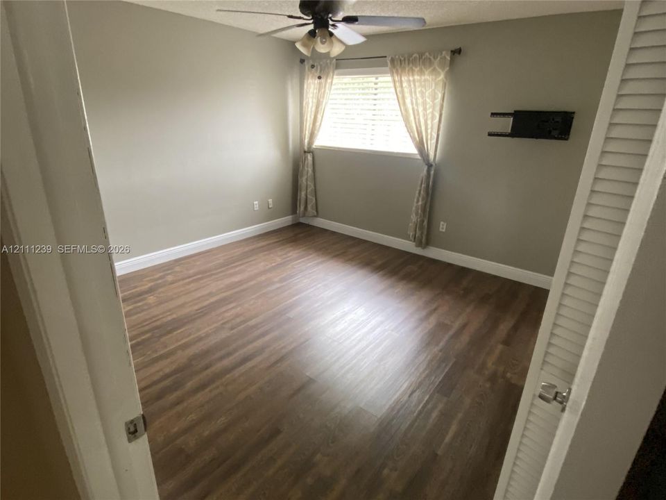Room featuring wood-finish flooring, a ceiling fan with integrated lighting, and a closet with louvered doors