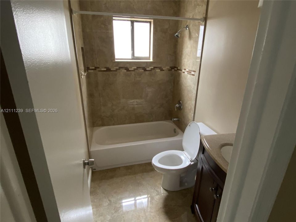 Bathroom featuring stone-finish wall tile with a decorative mosaic inlay, deep soaking tub, polished countertop, and dark-finish vanity cabinet