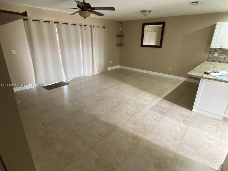 Large-format ceramic tile flooring, kitchen peninsula featuring light-toned countertop, white cabinetry with patterned backsplash, ceiling fan, and sliding glass door