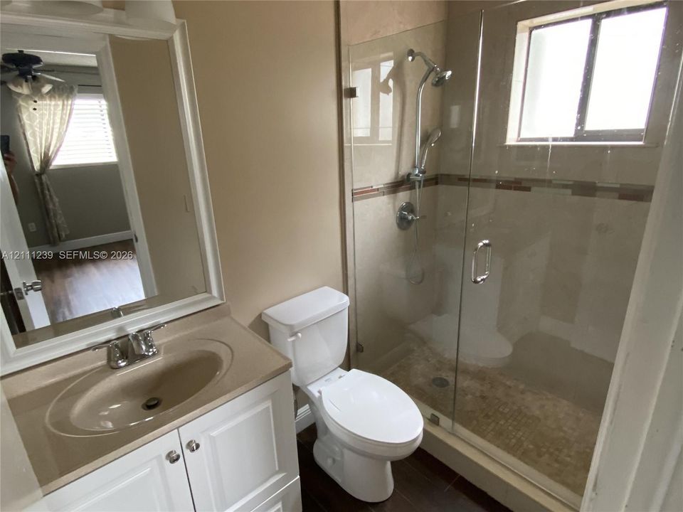 Bathroom featuring a vanity with an integrated sink, framed wall mirror, glass-enclosed shower with a handheld fixture, and wood-finish flooring