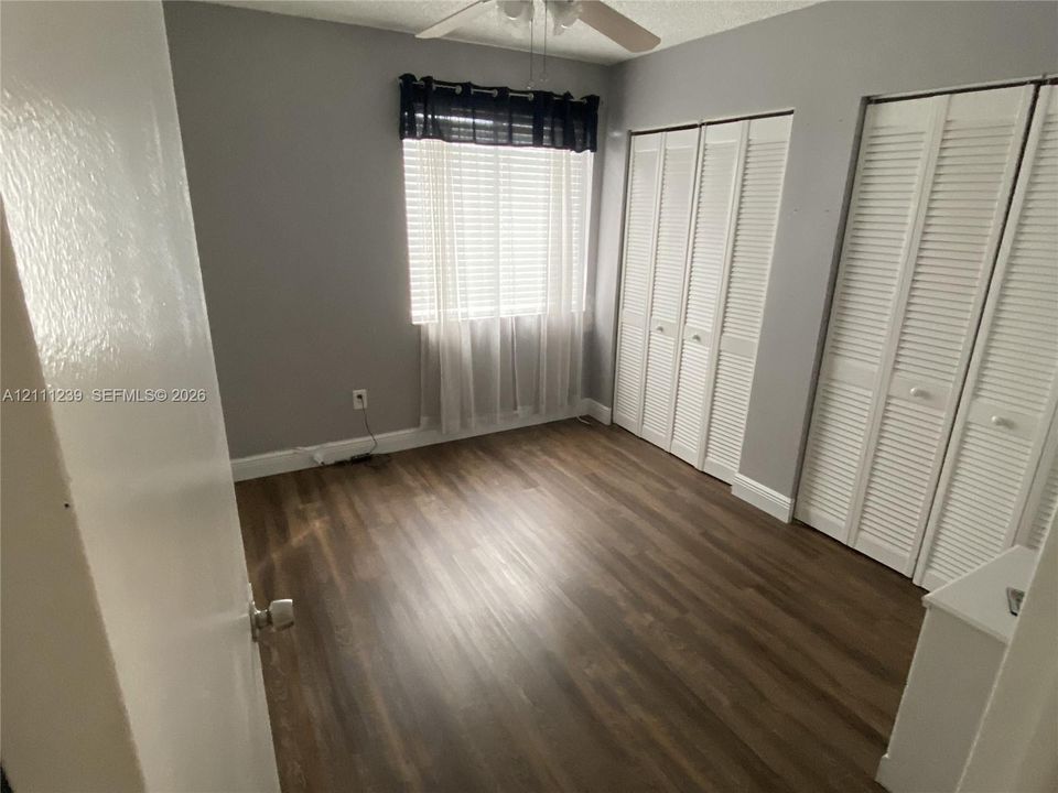 Room featuring wood-finish flooring, dual bi-fold louvered closets, a single-pane window, and a ceiling fan