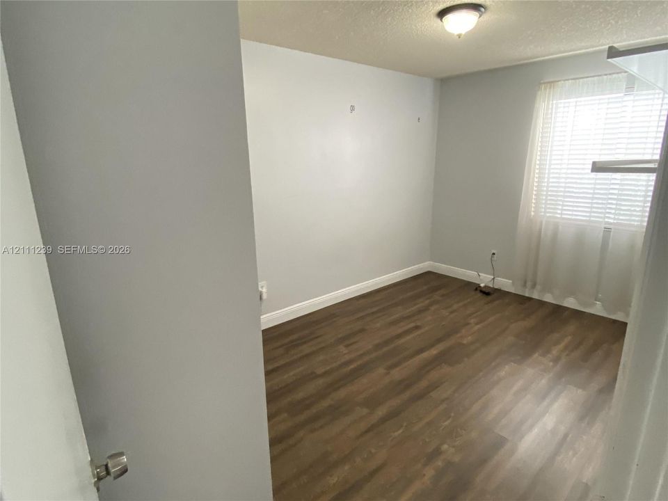 Wood-finish flooring, neutral wall tones, and window with horizontal blinds and drapery