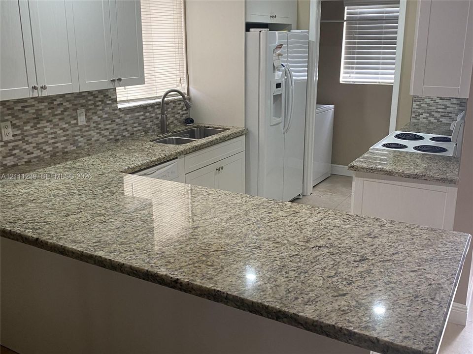 Kitchen featuring white cabinetry, stone countertops, a mosaic tile backsplash, a dual-basin stainless steel sink with an arched faucet, and a built-in cooktop