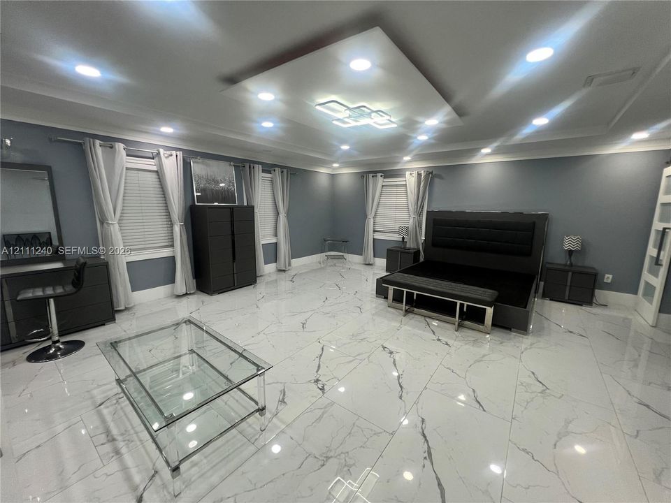 Large-format tile flooring with veining, recessed ceiling lighting, a tiered central ceiling fixture, and multiple windows