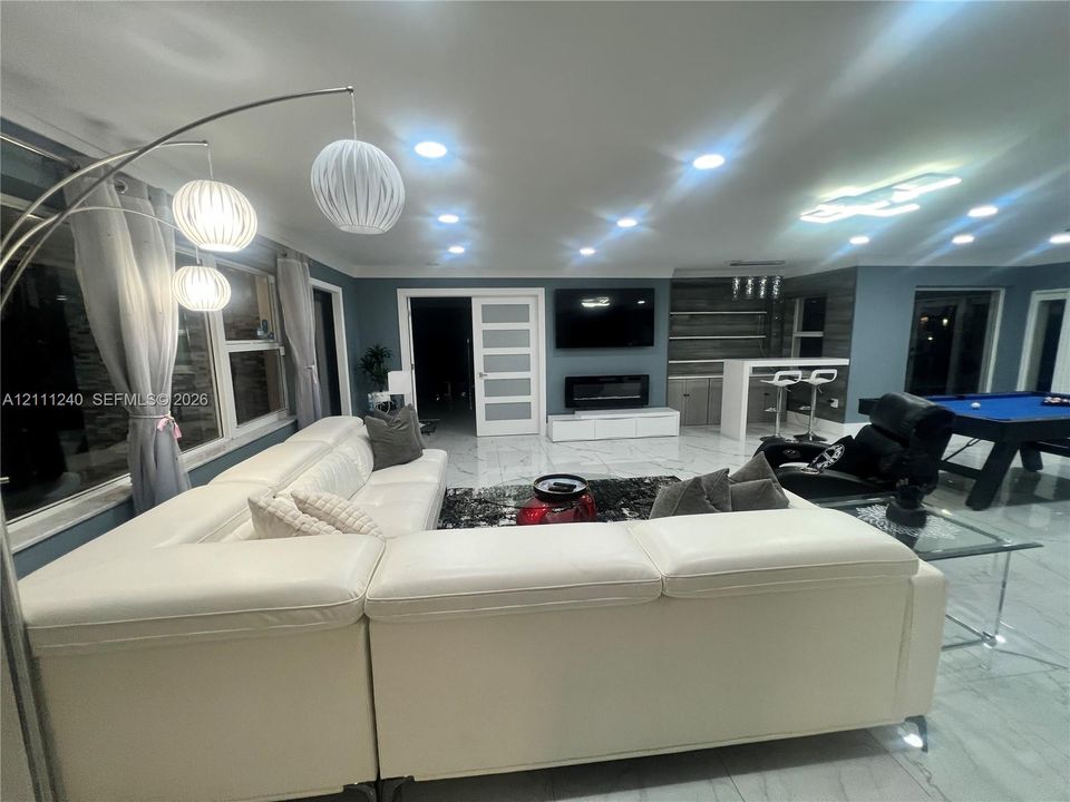 Large format tile flooring, recessed ceiling lighting, wall-mounted electric fireplace, built-in dry bar with shelving, and shaker-style interior door