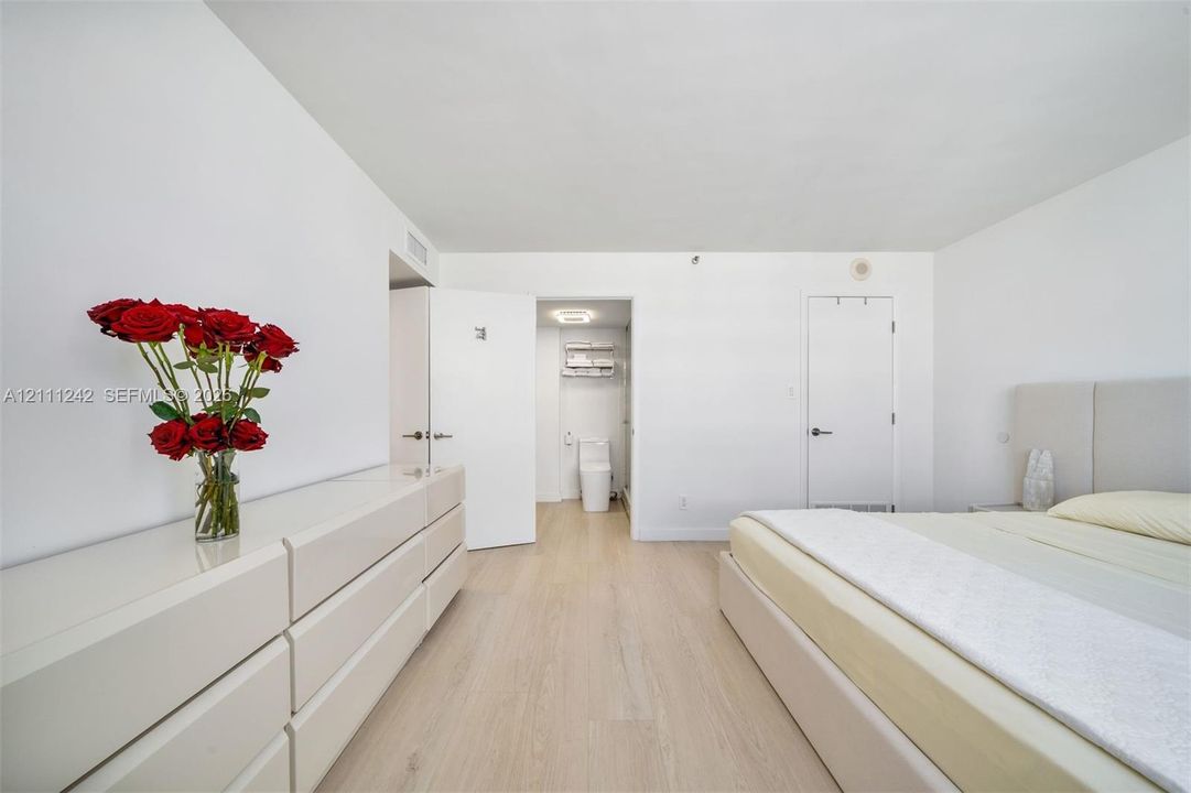 Bright interior featuring light-tone wood-finish flooring, smooth white walls, solid-core doors with matte black hardware, and an integrated bathroom fixture