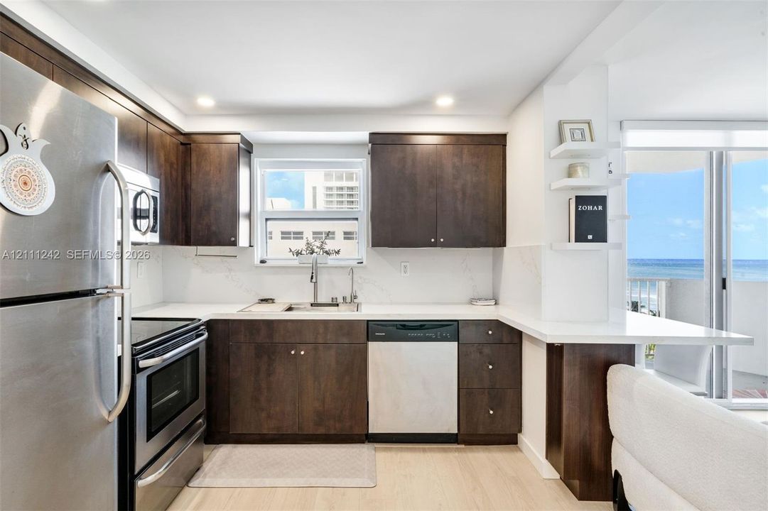 Kitchen featuring dark-finish cabinetry, quartz countertops, stainless steel appliances, floating shelves, and sliding glass doors with ocean exposure