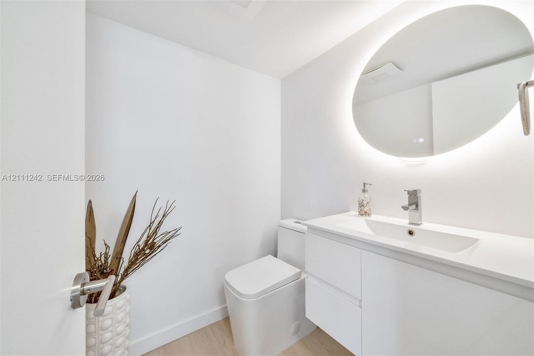 Modern floating vanity with an integrated rectangular sink, sleek white cabinetry, illuminated oval wall mirror, and minimalist water-saving toilet