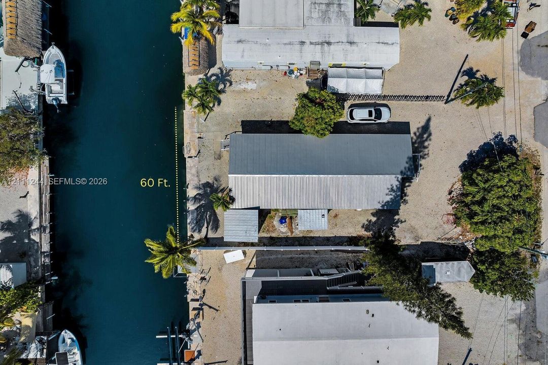 Aerial perspective of a waterfront property featuring 60 feet of canal frontage, a metal roof structure, and mature palms