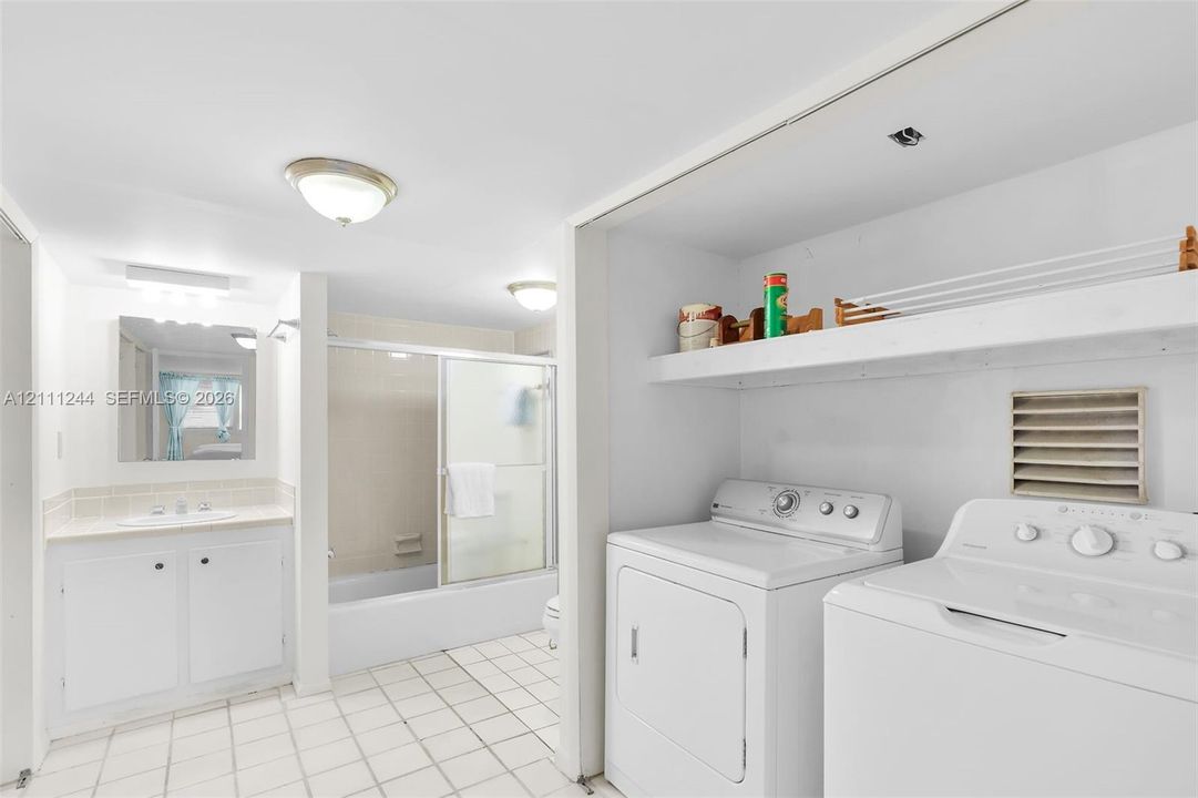 Bathroom featuring a vanity with integrated sink, tub-shower combination with sliding glass doors, ceramic tile flooring, and a dedicated laundry area with built-in shelving