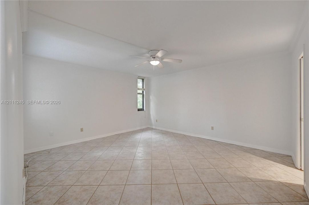 Spacious interior featuring light-colored tile flooring, neutral wall tones, a ceiling fan with integrated lighting, and a vertical window