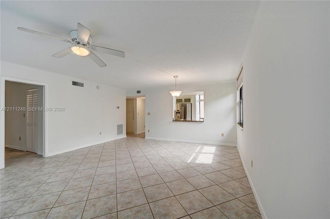 Open-concept interior featuring neutral tile flooring, white walls, a ceiling fan with integrated lighting, and a kitchen pass-through window with an attached counter