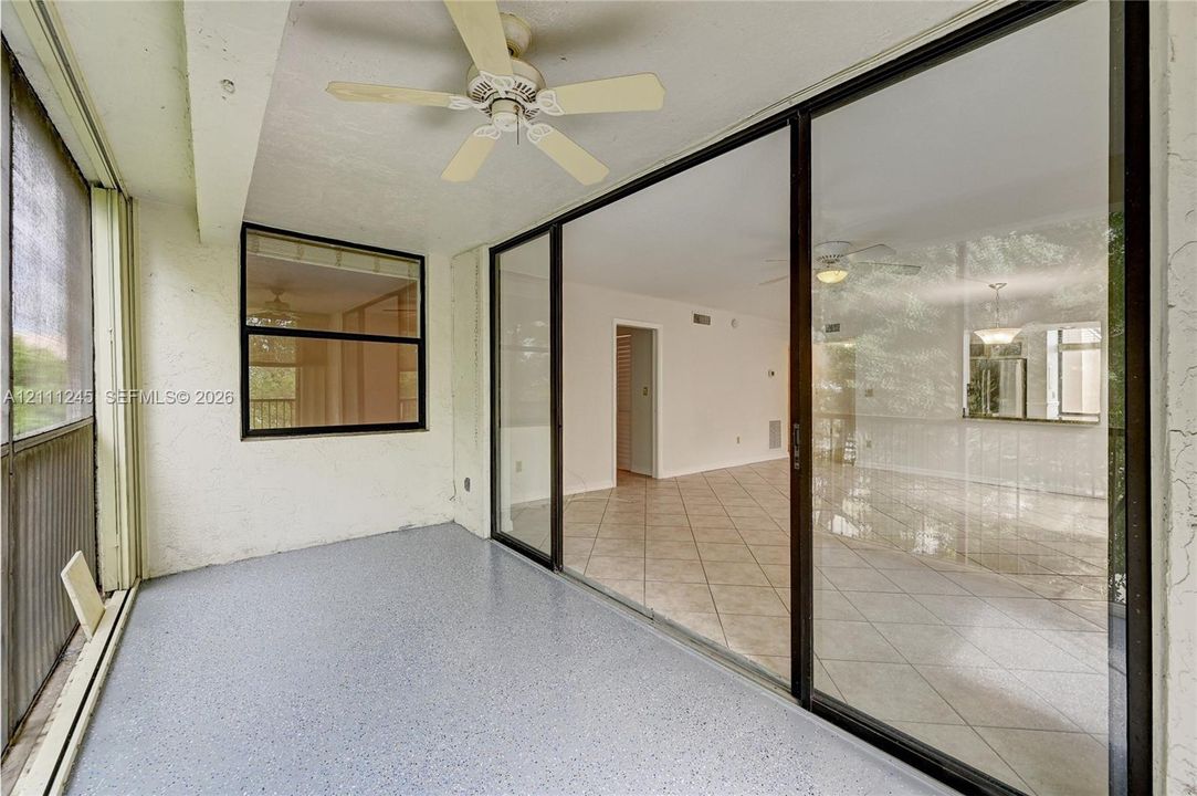 Screened-in porch featuring expansive glass sliding doors, painted concrete flooring, and a ceiling-mounted fan