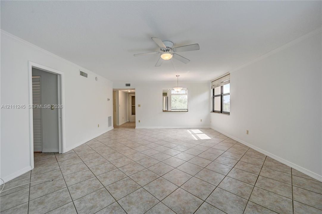 Open-concept interior featuring neutral tile flooring, a central ceiling fan with integrated lighting, a pass-through opening, and a large window with window treatments