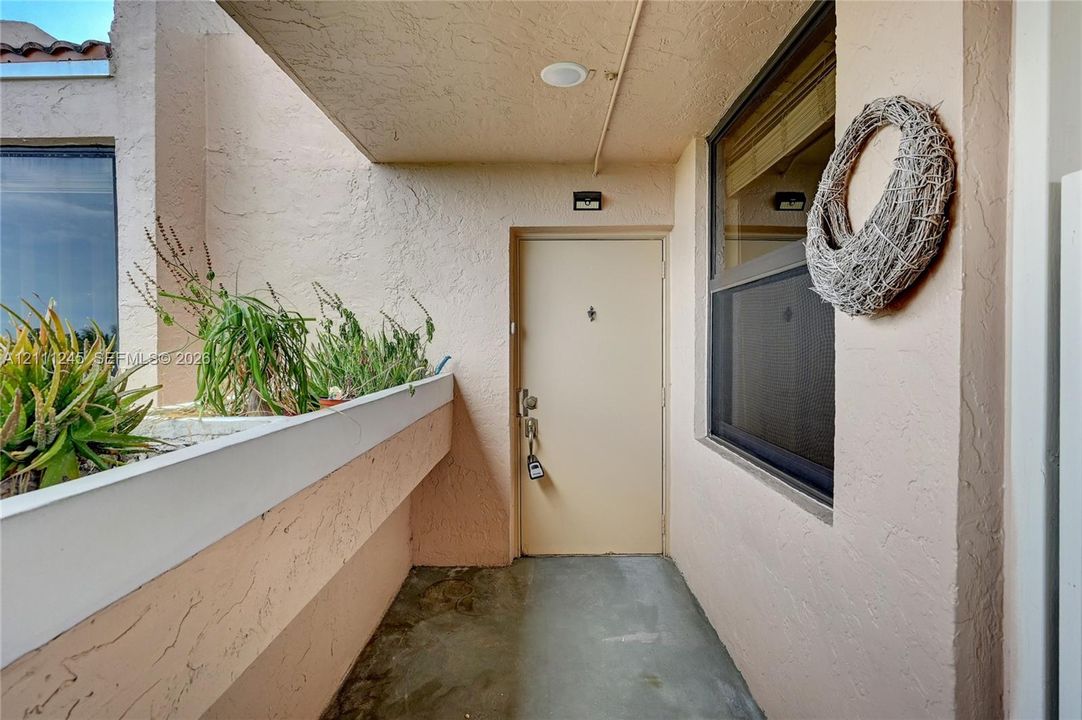 Covered entryway featuring textured stucco walls, a concrete floor, integrated recessed lighting, and a built-in stucco planter