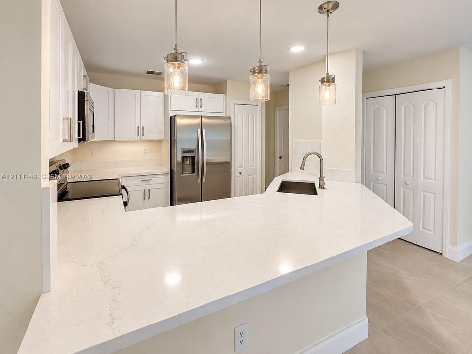 Kitchen featuring white cabinetry, quartz countertops, stainless steel appliances, a peninsula with an undermount sink, and three glass pendant lights