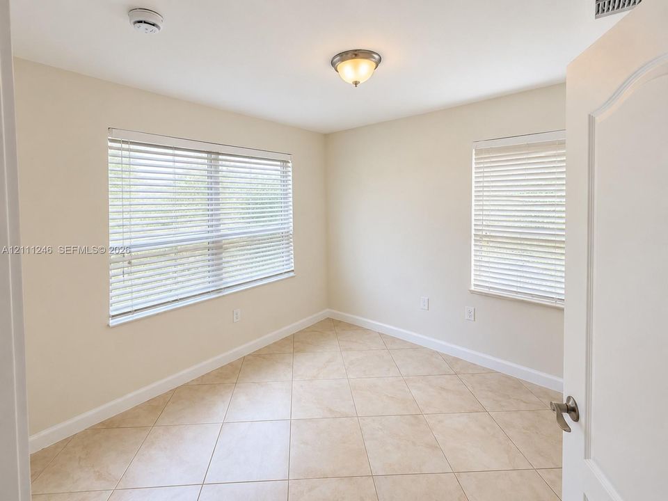 Neutral-toned room featuring diagonal tile flooring, dual windows with horizontal blinds, and a brushed nickel flush-mount ceiling light fixture