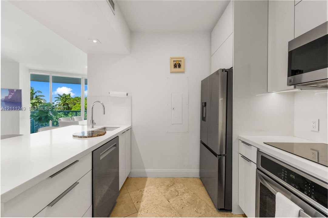 Kitchen featuring white flat-panel cabinetry, solid-surface countertops, stone-tile flooring, and stainless steel appliances