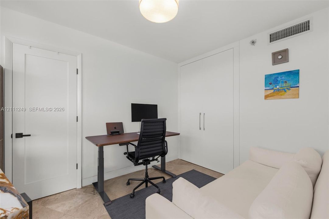 Interior space featuring stone-finish flooring, a solid-core door with matte black hardware, built-in floor-to-ceiling storage cabinetry, and a flush-mount ceiling light fixture