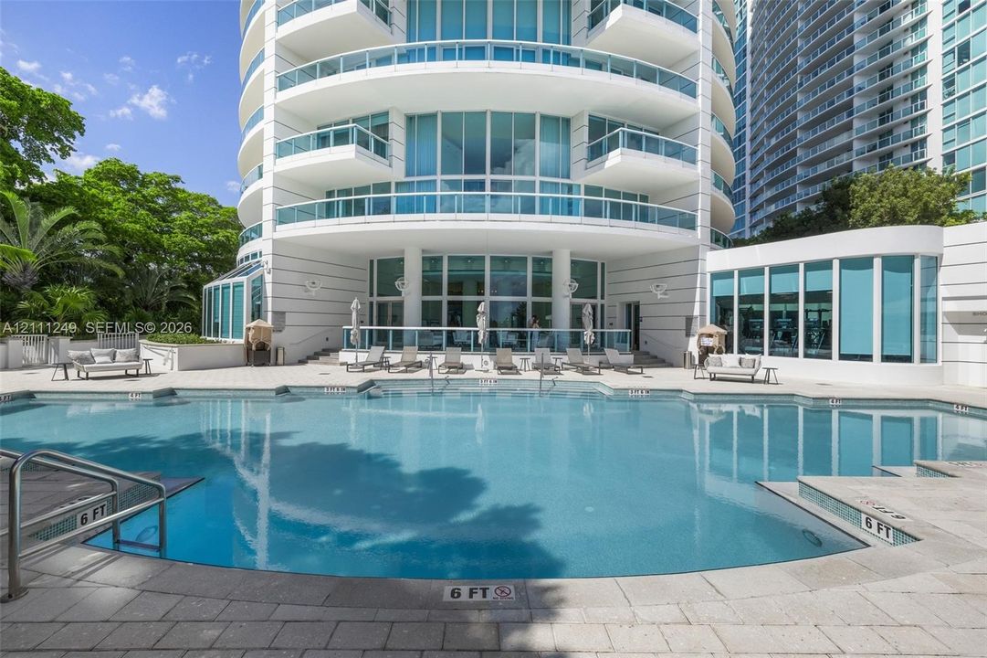 Swimming pool with concrete paver decking, multi-story tower facade, glass-paneled balconies, and floor-to-ceiling glass wall architecture