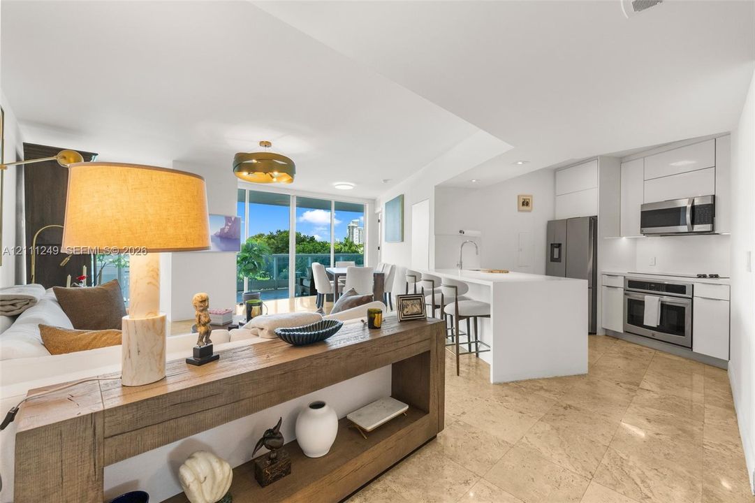 Open concept interior featuring stone-tile flooring, sleek white flat-panel cabinetry, a stainless steel appliance suite, and a waterfall-edge kitchen island