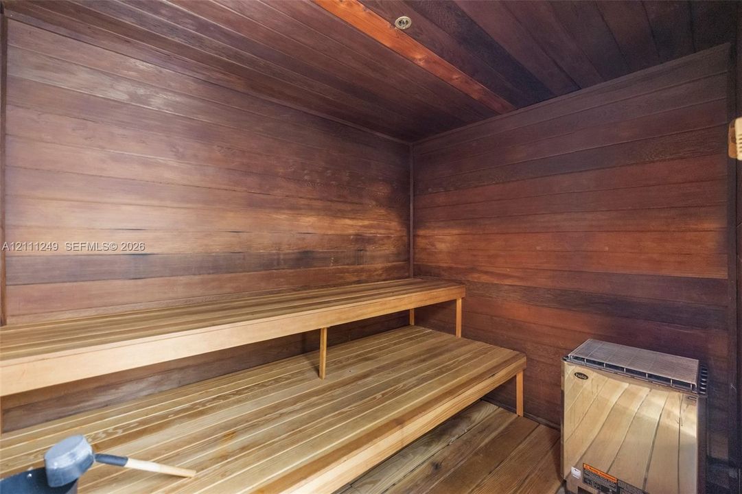 Sauna featuring natural wood-plank wall paneling, multi-level slatted benches, and a dedicated heating unit