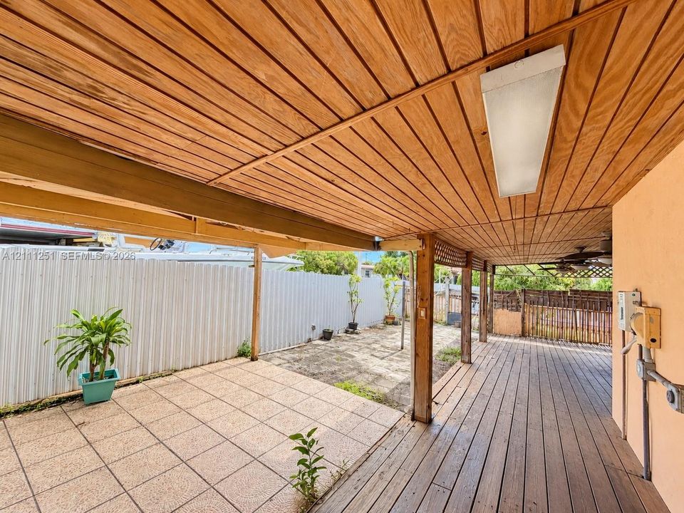 Covered patio featuring a wood-plank ceiling, wood-finish decking, tiled hardscaping, and structural support beams