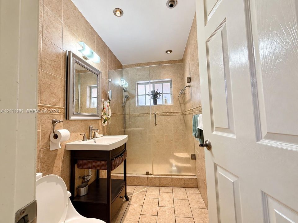 Bathroom featuring floor-to-ceiling ceramic tile, a glass-enclosed shower, a pedestal vanity with integrated storage, and recessed lighting