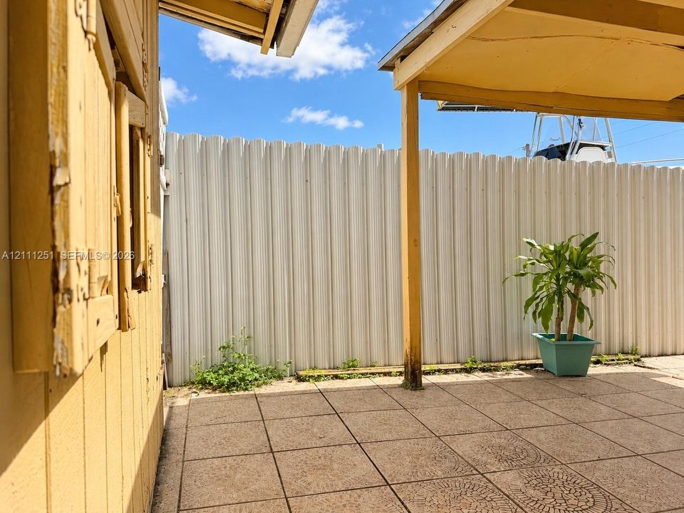 Covered patio area featuring square tile flooring and a corrugated metal perimeter privacy fence