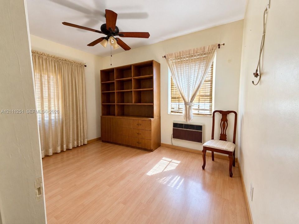 Wood-finish flooring, built-in wooden shelving unit, ceiling fan with light fixture, and window-mounted air conditioning unit