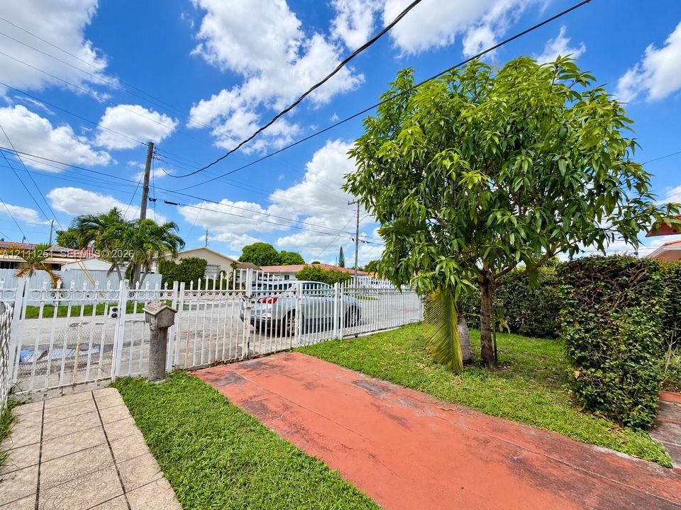 Exterior grounds featuring a paved driveway, decorative metal perimeter fencing with gate, and established landscaping including a mature tree and manicured shrubbery
