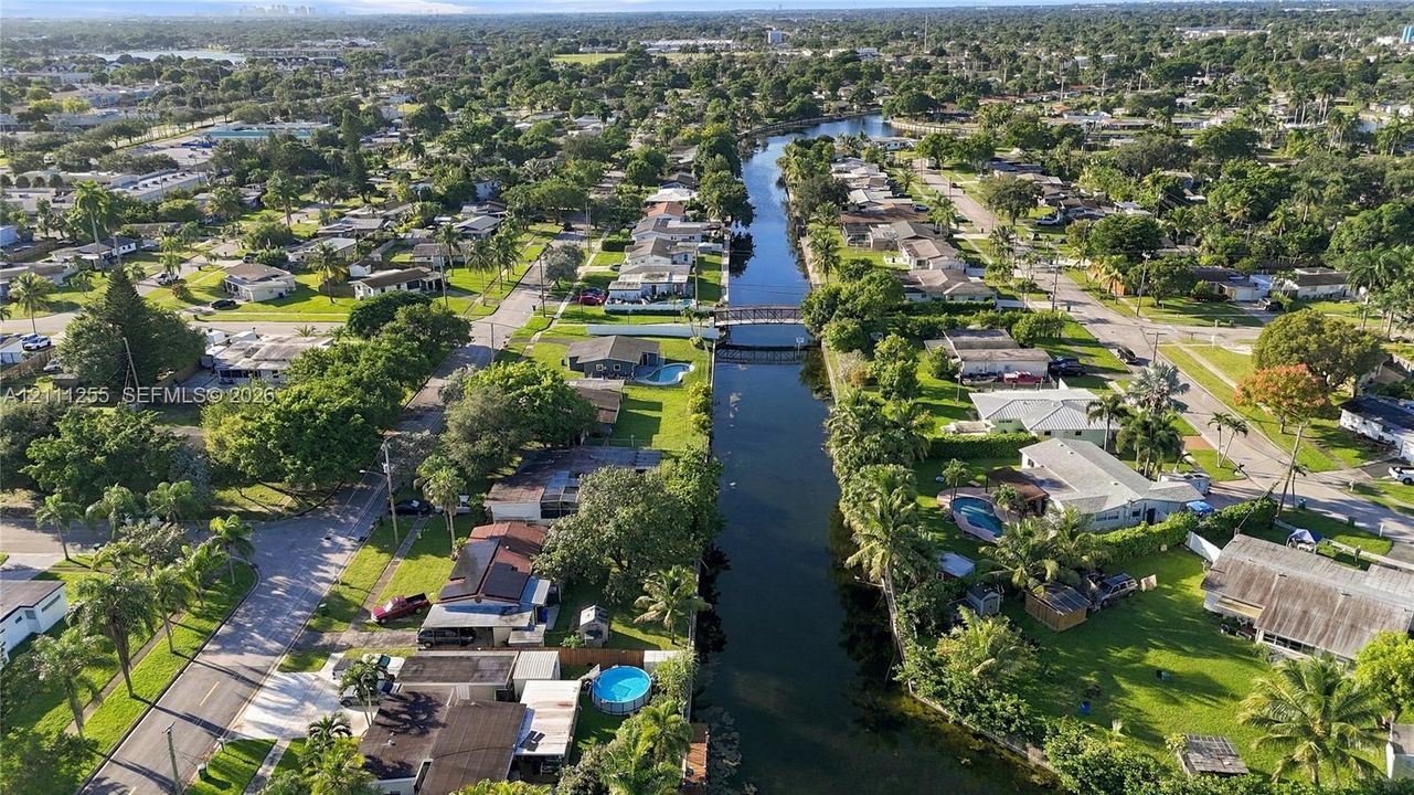 Aerial perspective of a canal-front property featuring mature vegetation and established residential landscaping