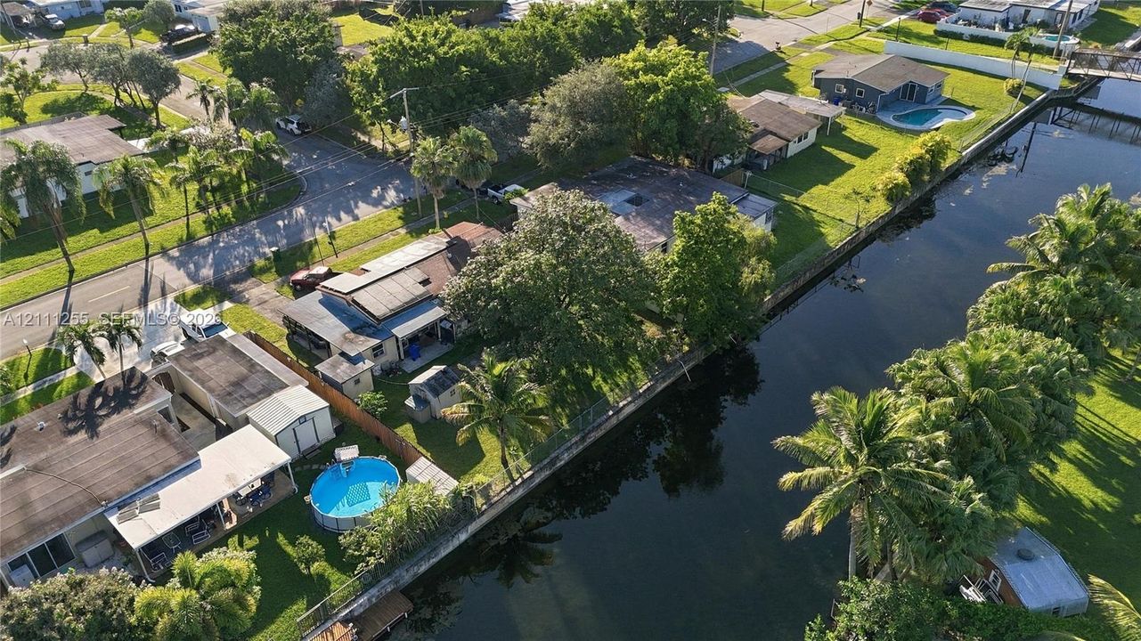 Canal-front property featuring a detached swimming pool, mature palms, and fenced perimeter