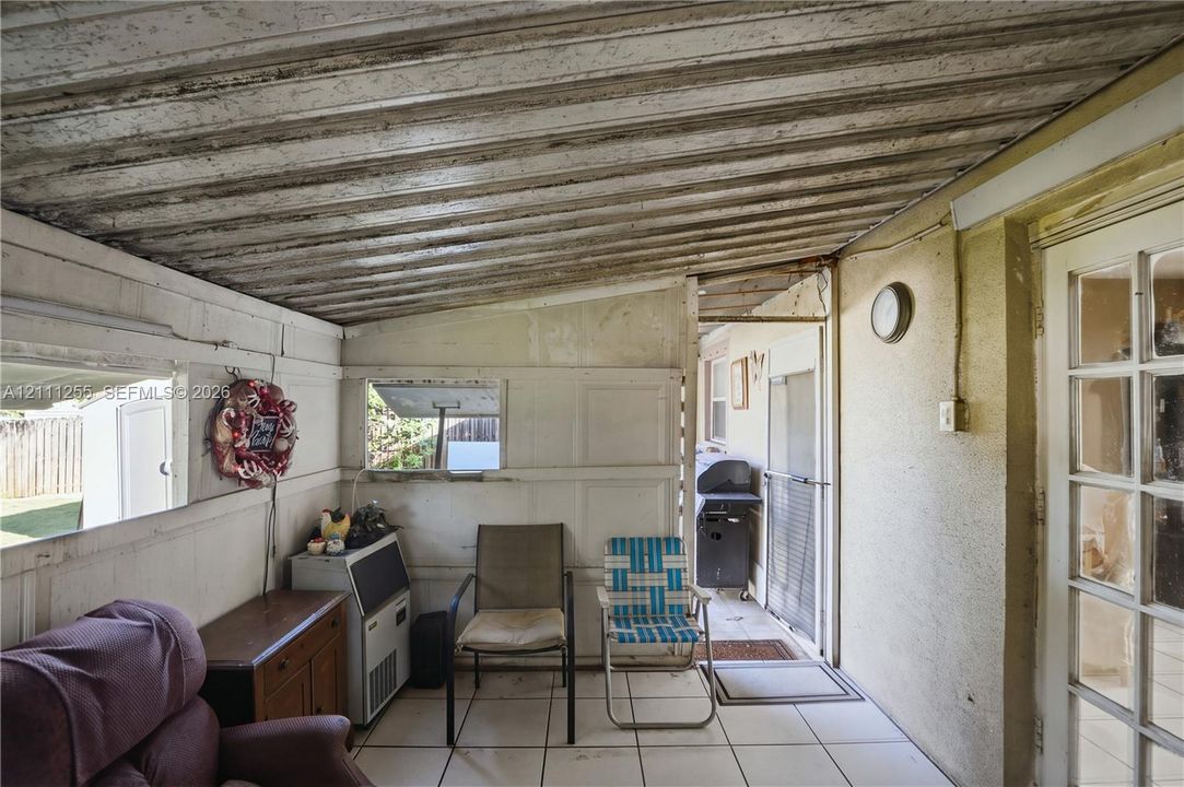 Enclosed patio featuring a corrugated metal ceiling, ceramic tile flooring, horizontal sliding windows, and a glass-paneled exterior door