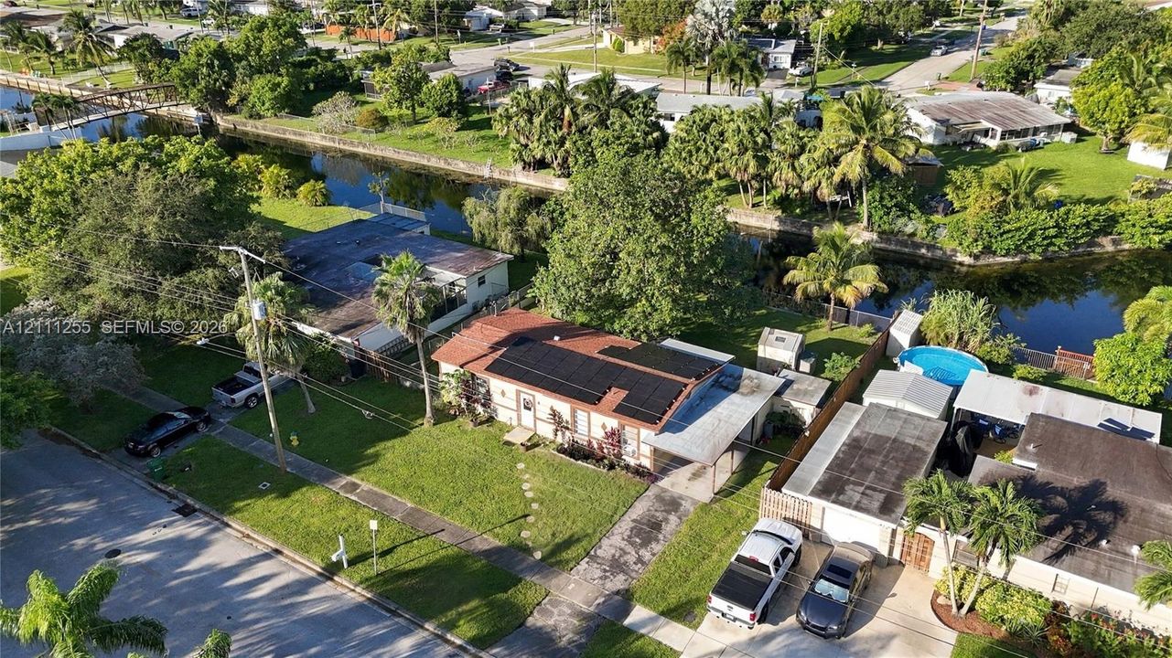Aerial perspective of a single-story residence featuring solar panels, a concrete driveway, an attached carport, and a backyard canal