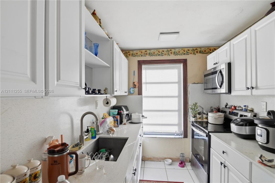 Kitchen featuring white shaker-style cabinetry, solid-surface countertops, a stainless steel undermount sink, ceramic tile flooring, and a built-in stainless steel microwave