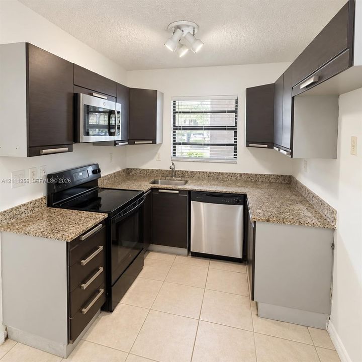 Kitchen featuring dark cabinetry, stone-finish countertops, stainless steel appliances, tile flooring, and multi-light ceiling fixture