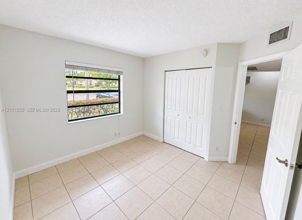 Neutral-toned room featuring tile flooring, a large single-pane window, and a built-in closet with double bifold doors