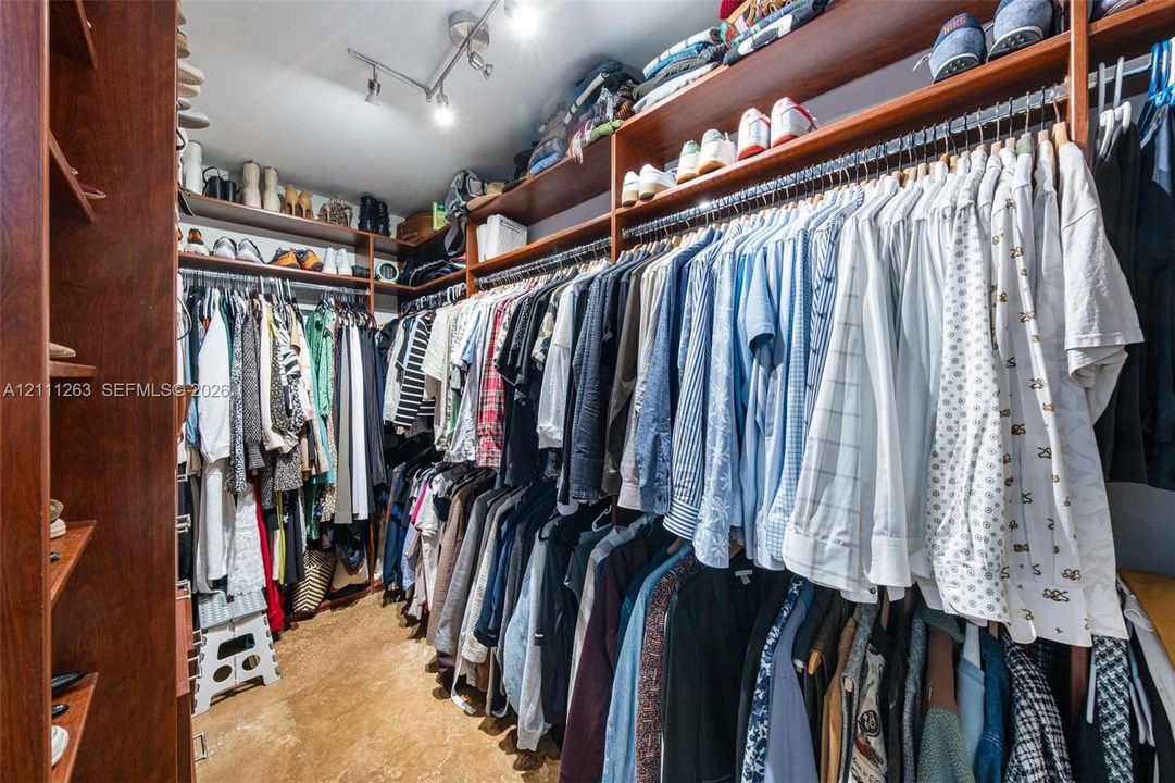Walk-in closet featuring extensive wall-to-wall wood-finish cabinetry, tiered hanging rods, multiple open storage shelves, and ceiling-mounted directional track lighting