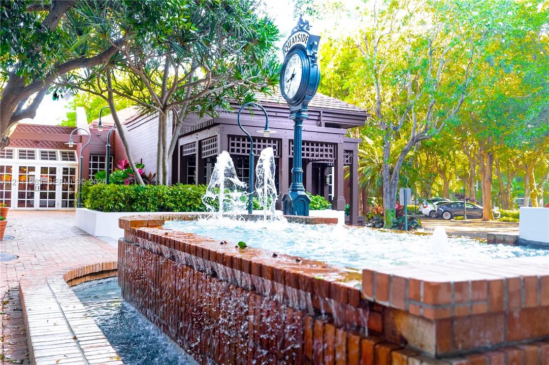 Tiered brick fountain with integrated water jets, decorative street-style clock, brick-paved walkways, and established landscape foliage